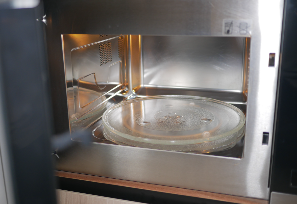 Open microwave interior with a glass plate and metal walls.