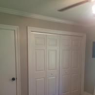 A white standard door and a white bifold closet door set against beige walls with white crown molding.
