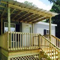 Wooden deck and covered porch with a metal roof attached to the side of a grey mobile home.