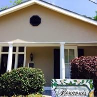 Tan house exterior with white columns and a painted sign reading 