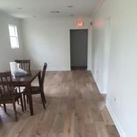 A dining table with two wooden chairs in a minimalist room with light wood-look flooring and white walls.