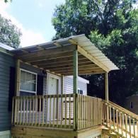 A new wooden porch and roof addition attached to a gray siding house, with a wooden railing and a ramp leading up.