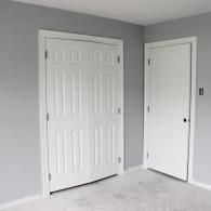 A white double-door closet and a single white door set into gray walls above a light-colored carpet.