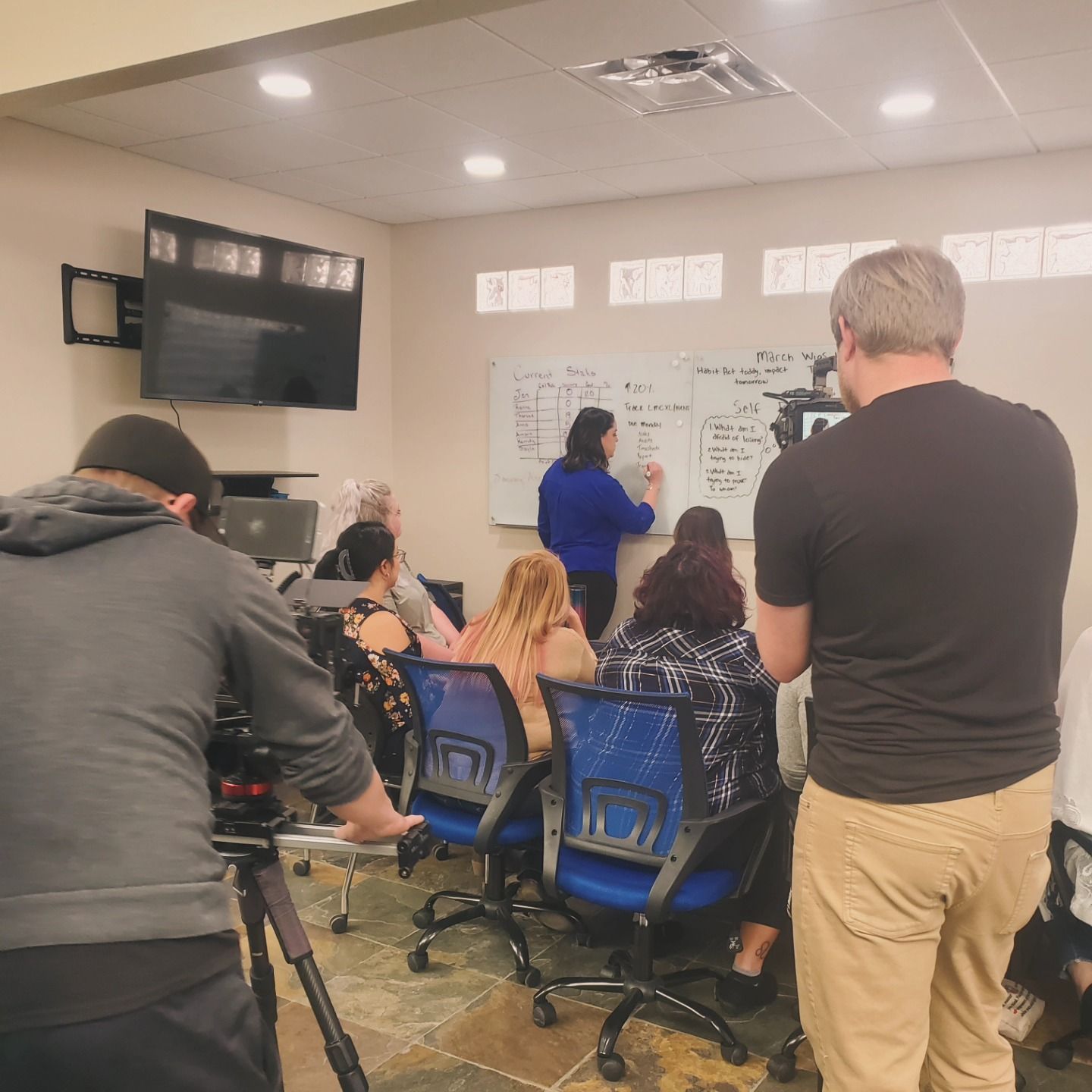 A group of people sitting in chairs in front of a white board