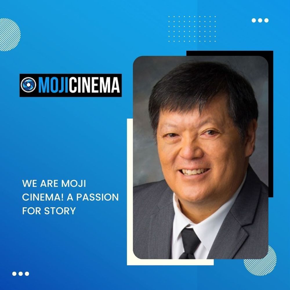 A man in a suit and tie is smiling in front of a blue background that says mojicinema