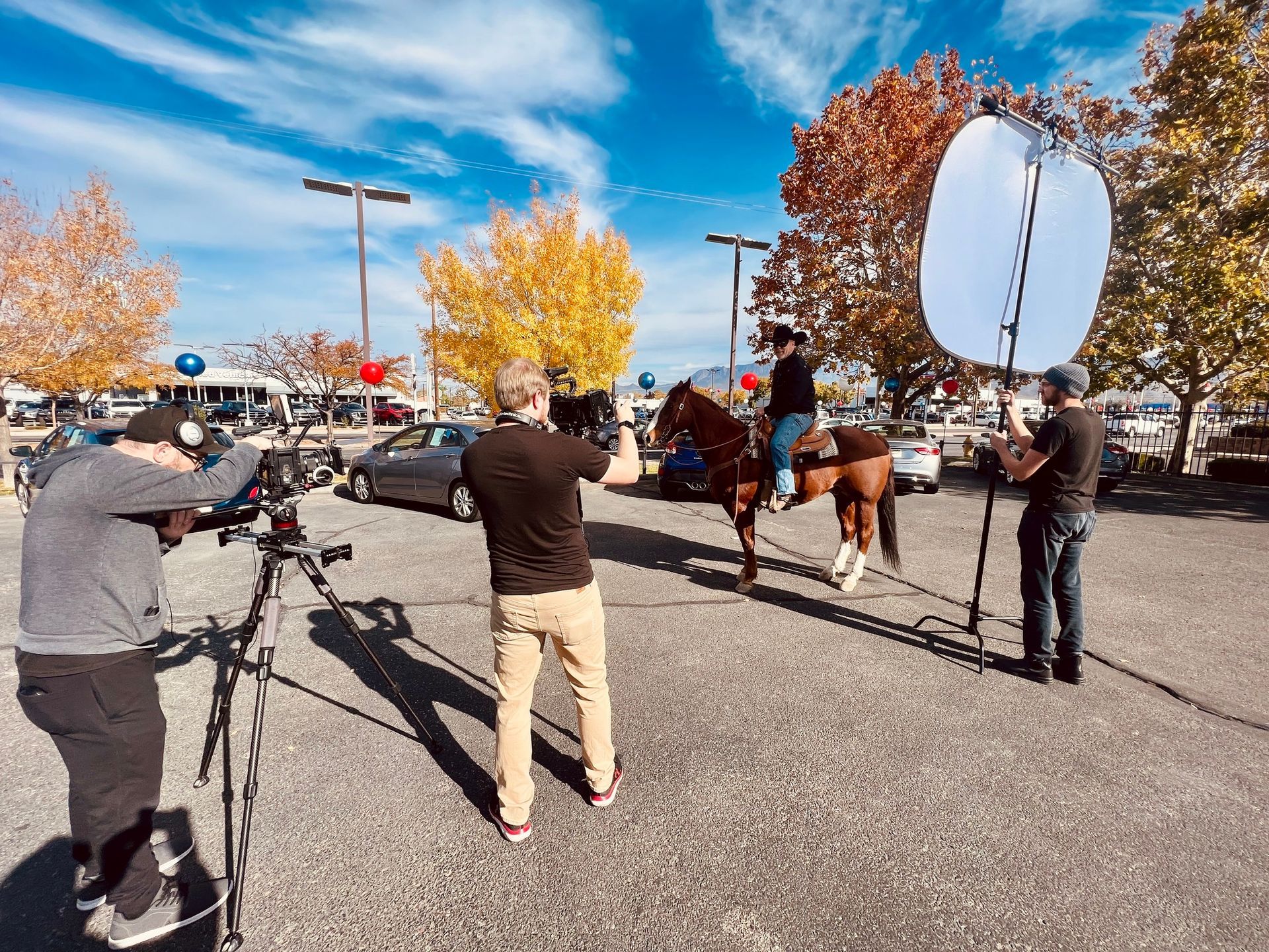 A man riding a horse is being filmed in a parking lot.