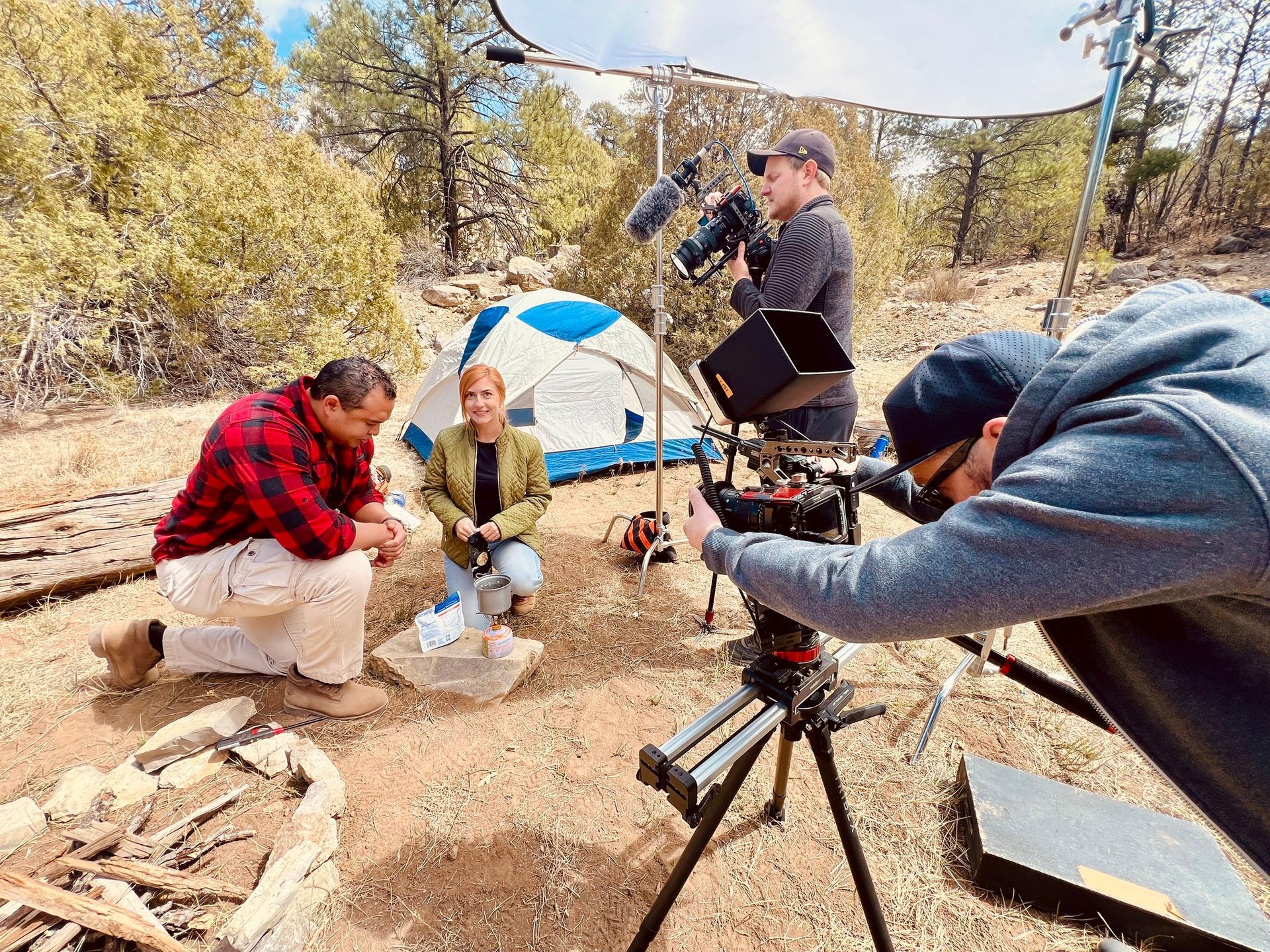 A group of people are sitting around a campfire while a man takes a picture with a camera.