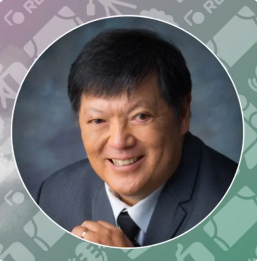 Man in a suit smiling, in a circular frame, with a blurred background.