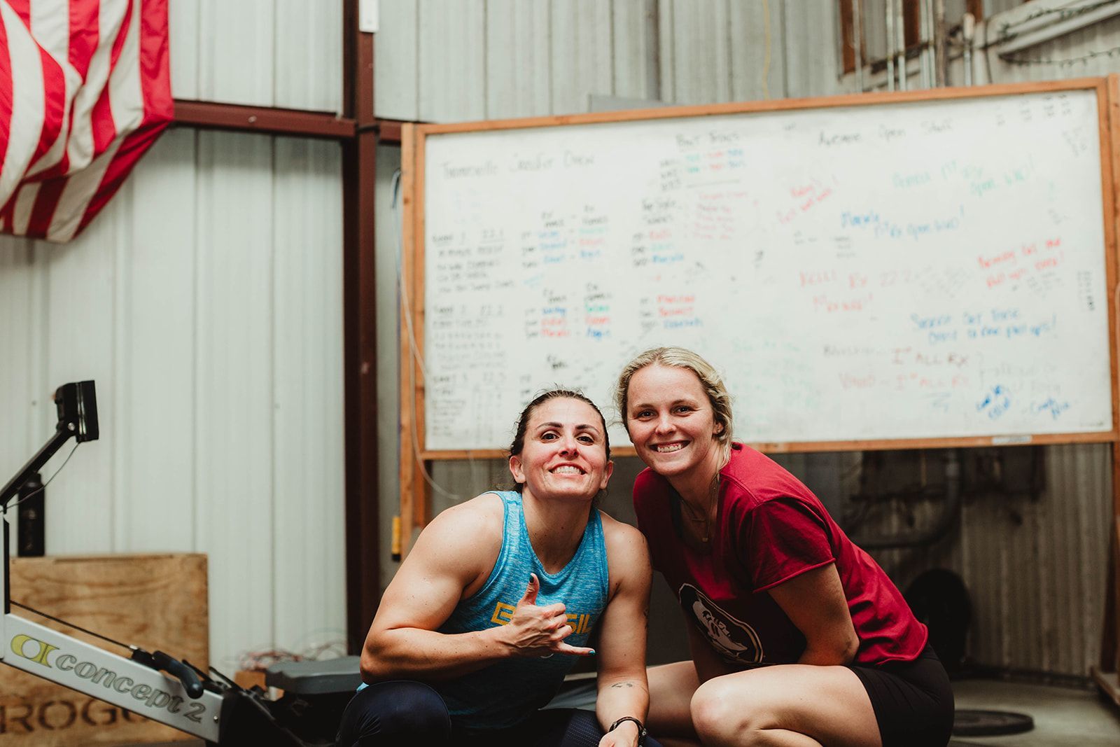 Two women are posing for a picture in front of the gym whiteboard at Rose City Barbell Club in Thomasville, GA