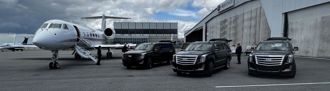 Private jet on tarmac with black SUVs. Cloudy sky. Airport hangar in background.