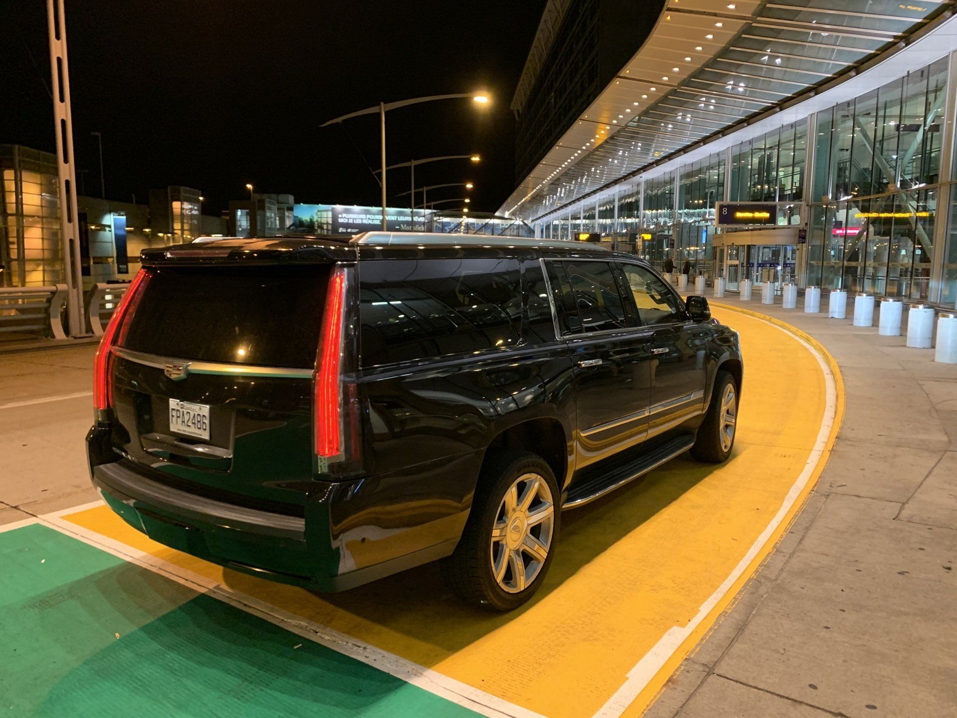 Black SUV parked at an airport terminal at night; yellow and green pavement.
