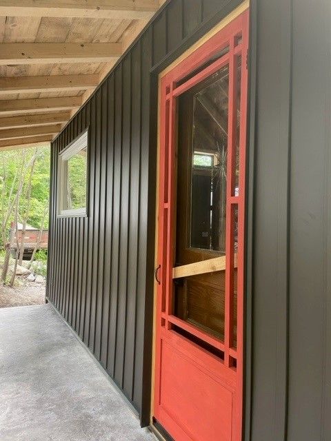 Intérieur d'un bâtiment avec murs en tôle ondulée grise, porte rouge et plafond en bois.