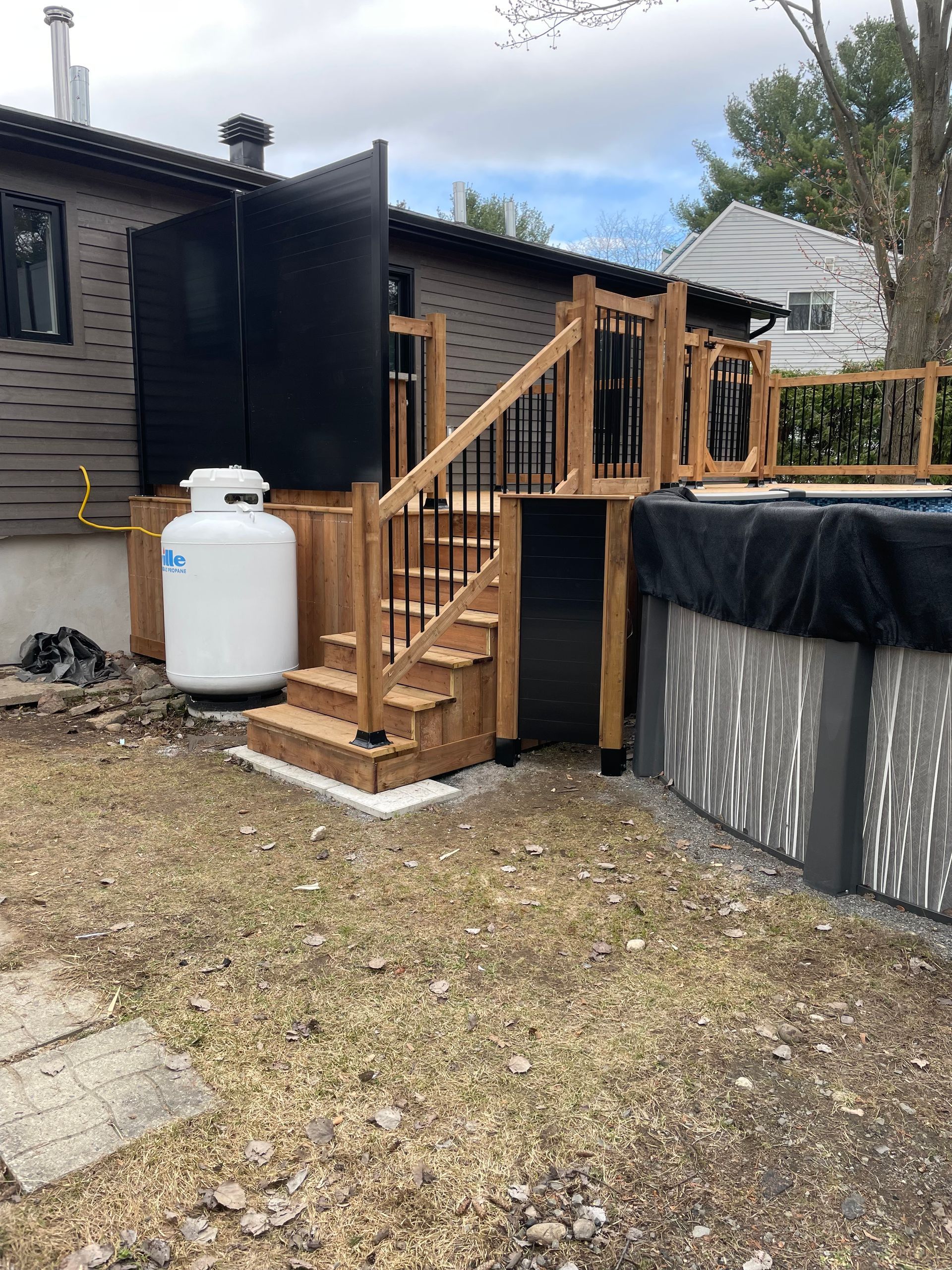 Une terrasse en bois avec des escaliers et un réservoir de propane devant une maison.