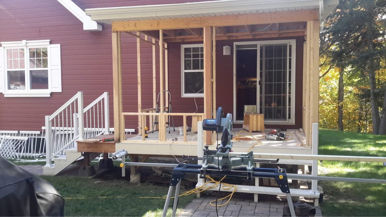 Un porche en bois est en construction devant une maison rouge.
