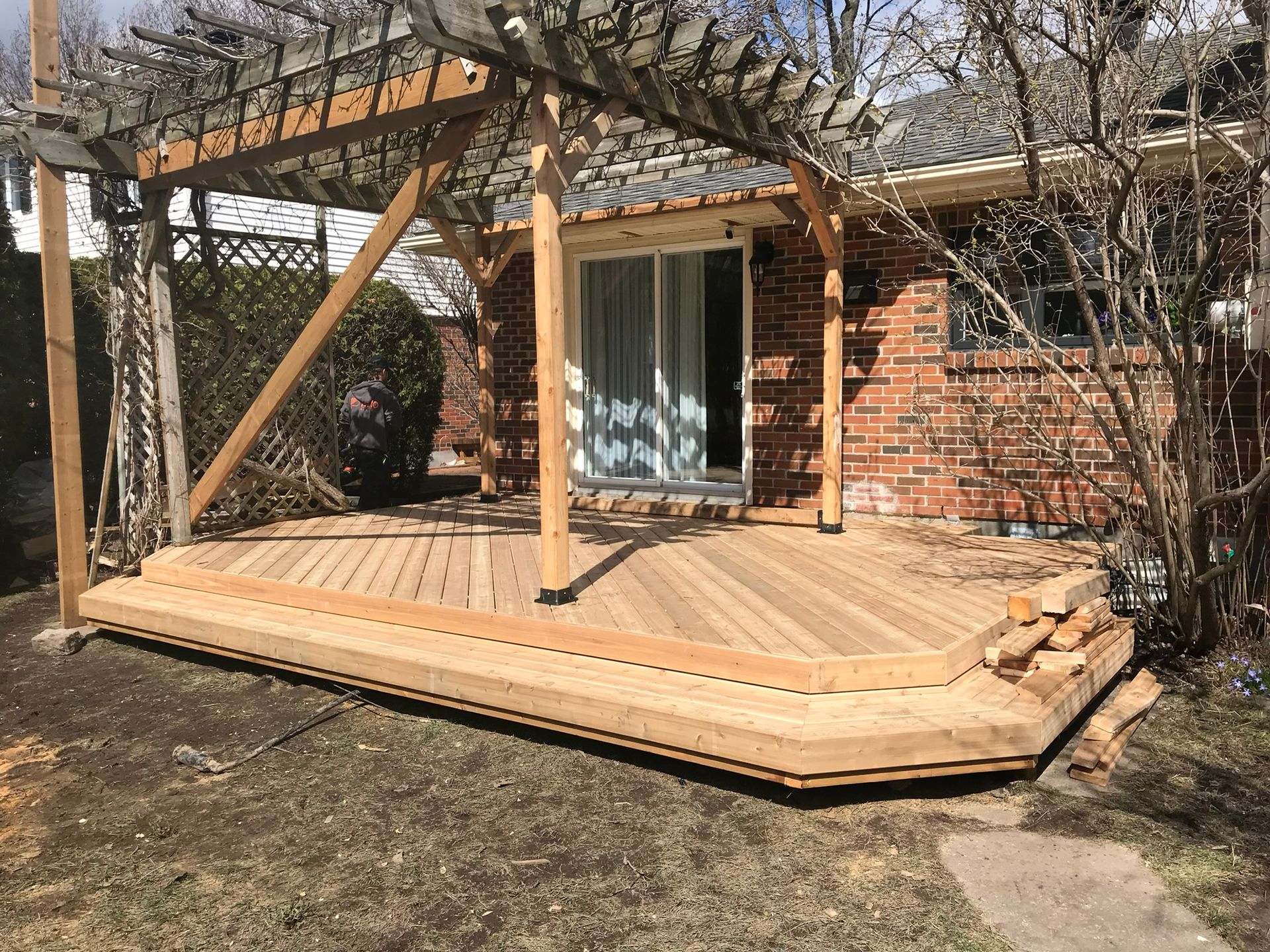 Terrasse en bois neuve avec pergola adoss&eacute;e &agrave; une maison en brique.
