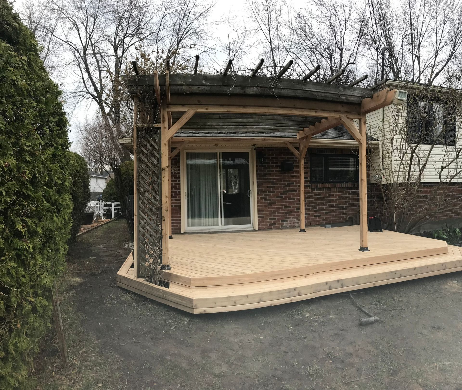Une terrasse en bois surmontée d'une pergola se trouve devant une maison en brique.