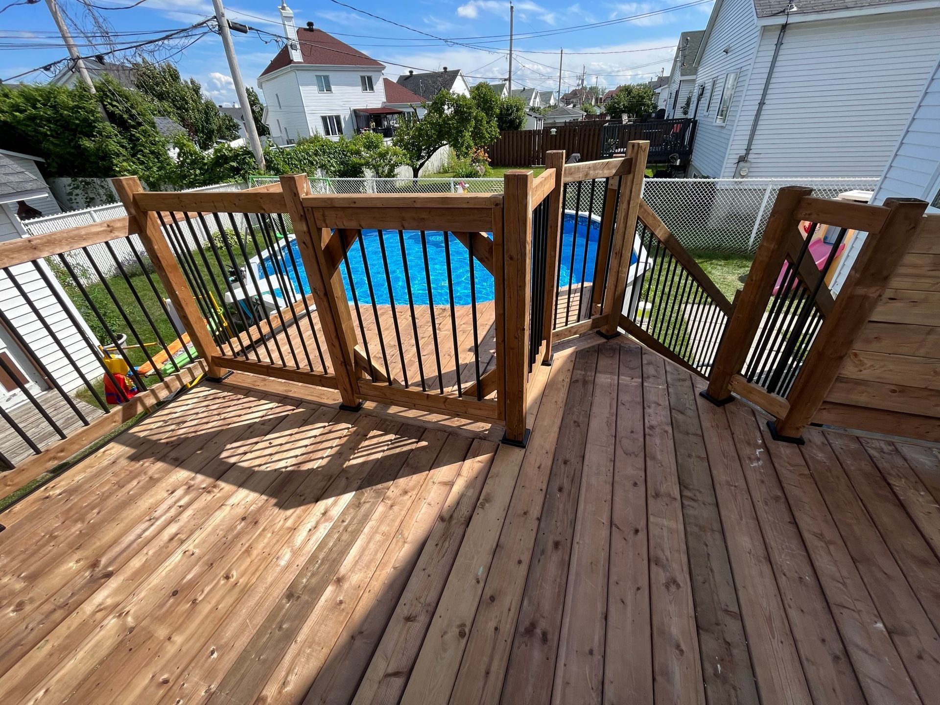 Une terrasse en bois avec un portillon de sécurité donnant sur une piscine hors-sol circulaire bleue dans un jardin résidentiel.