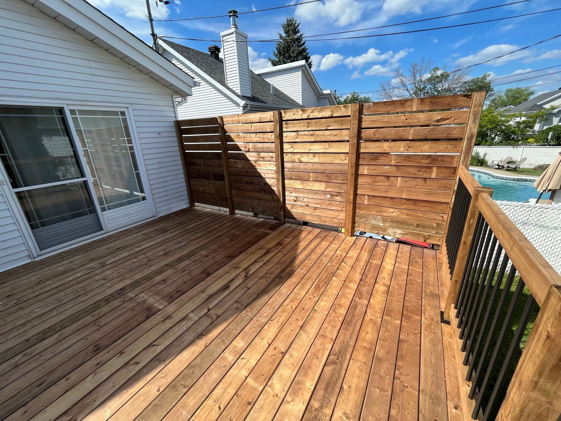 Terrasse en bois avec cl&ocirc;ture d'intimit&eacute; et rampe, adjacente &agrave; une maison blanche.