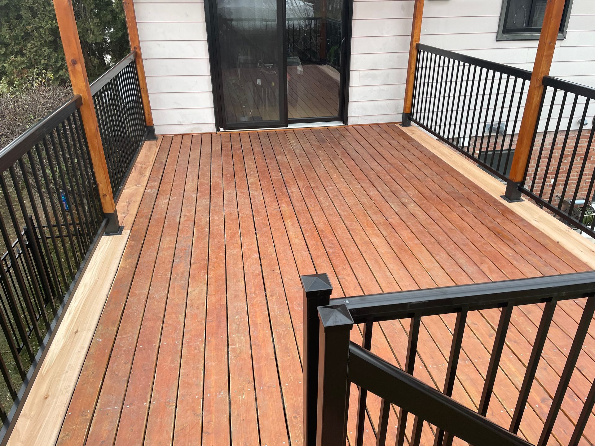 Terrasse en bois avec rampes noires et poteaux orange adjacente &agrave; une porte-fen&ecirc;tre.
