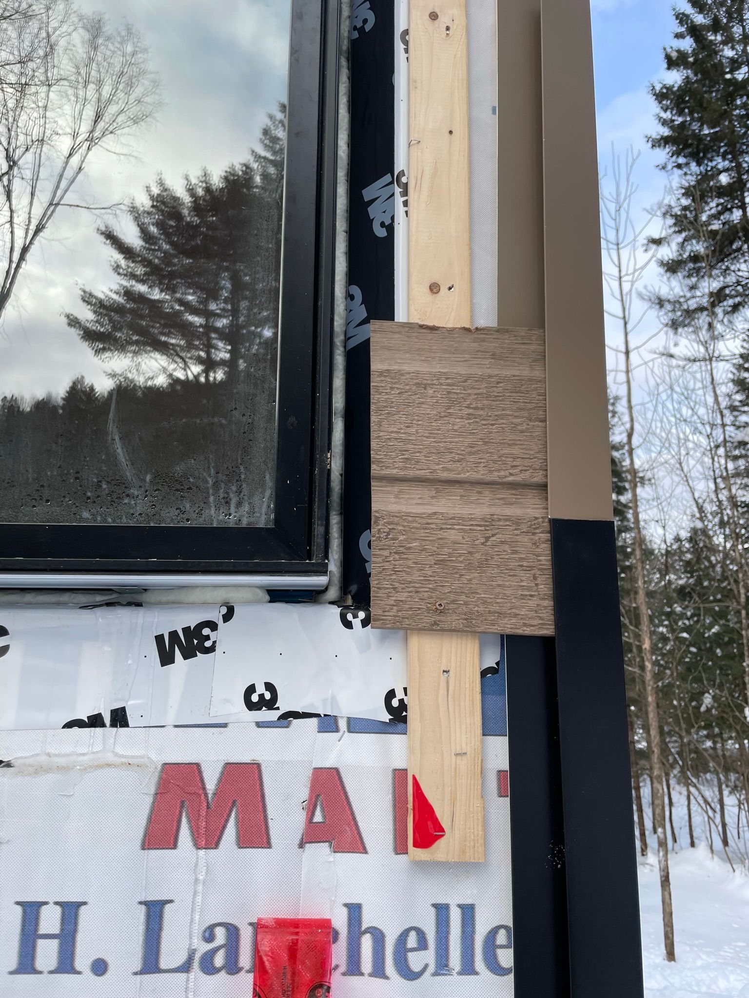D&eacute;tail d'installation de rev&ecirc;tement ext&eacute;rieur avec cadre de fen&ecirc;tre, bois et mat&eacute;riaux isolants visibles.