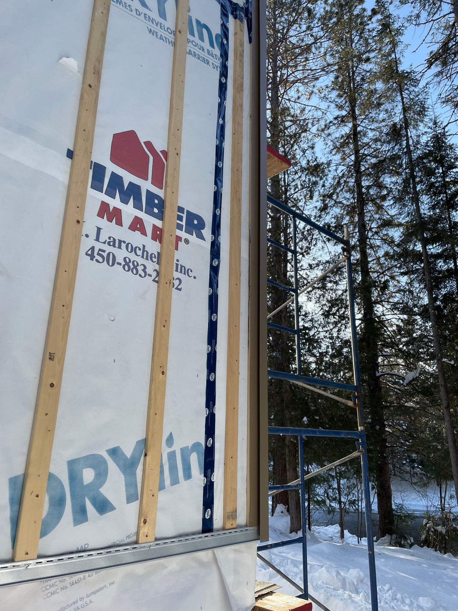 Panneau de rev&ecirc;tement blanc avec logo et num&eacute;ro de t&eacute;l&eacute;phone install&eacute; sur une structure en chantier.