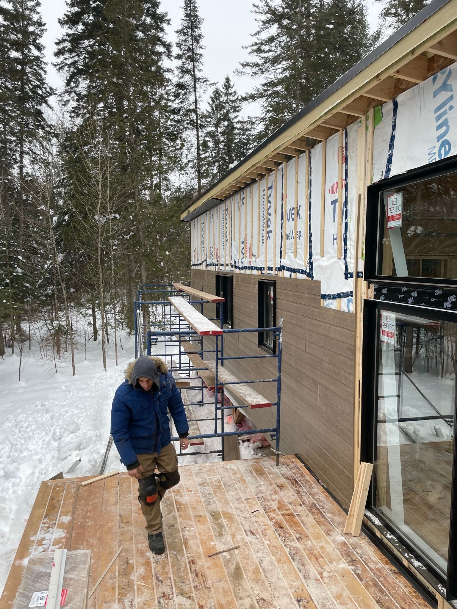 Un homme se tient sur une terrasse en bois devant un bâtiment en construction.