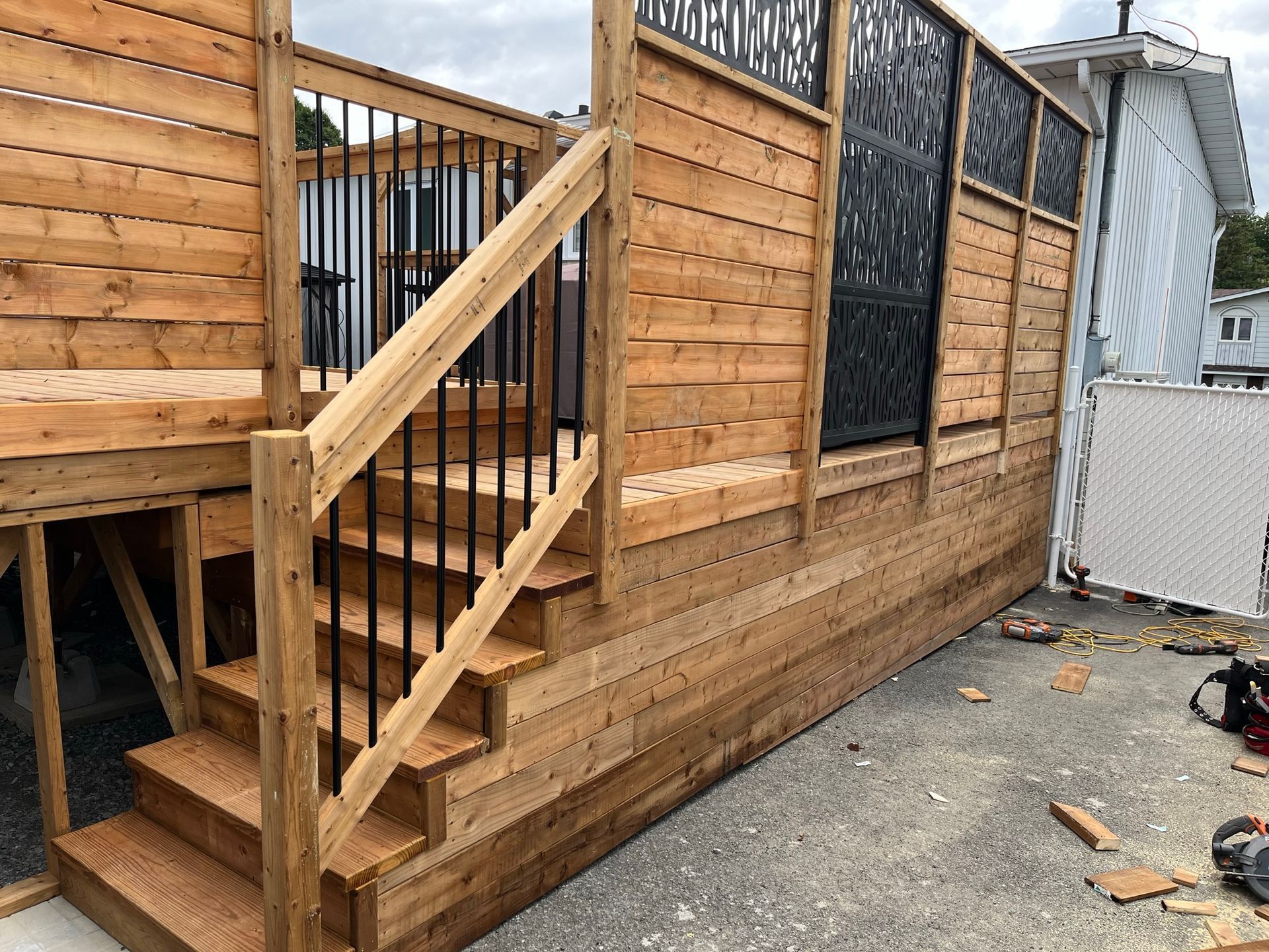 Terrasse en bois nouvellement construite avec escalier et clôture d'intimité ornée de panneaux métalliques décoratifs, aménagée dans un espace extérieur.