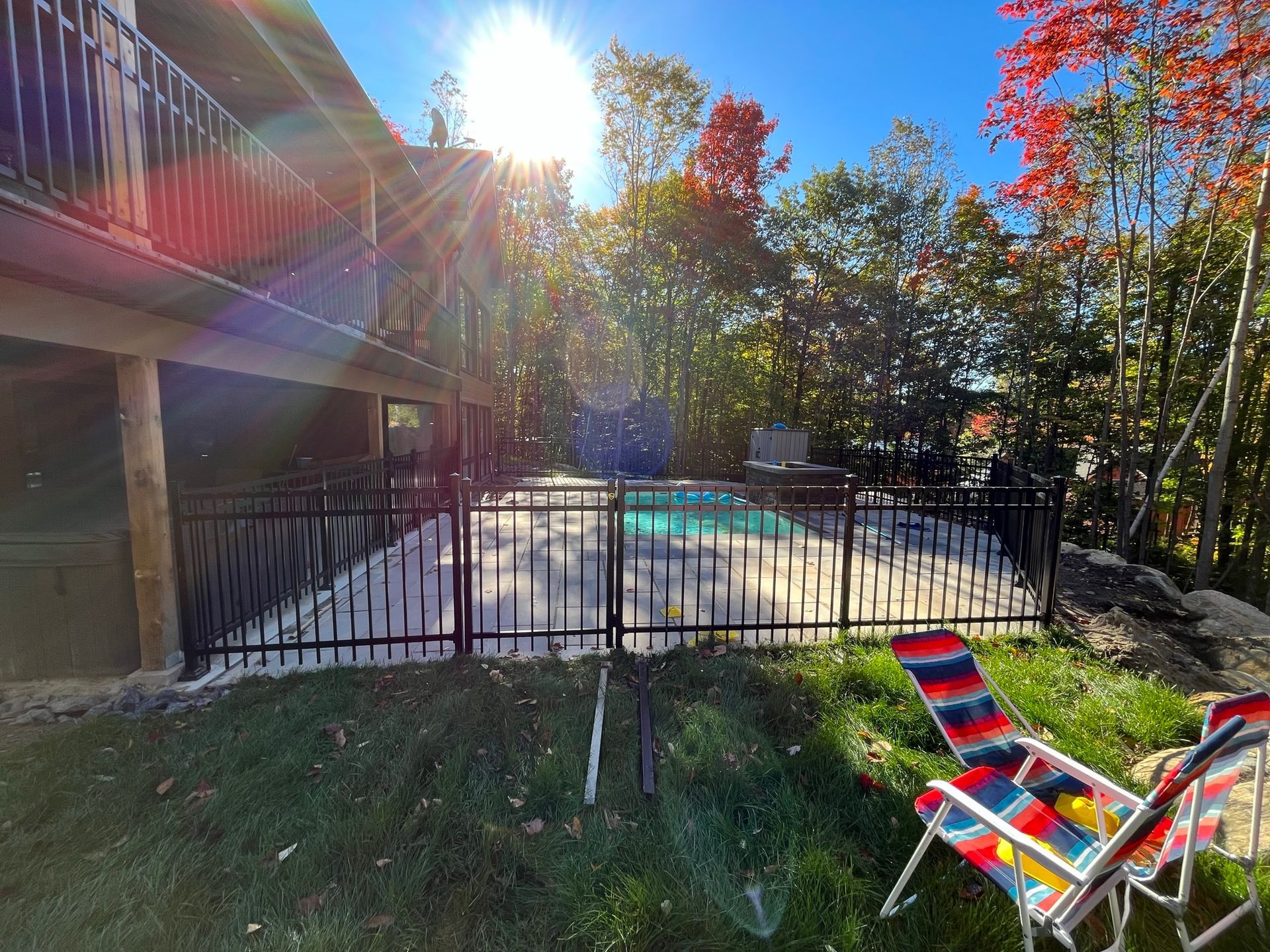 Une piscine se trouve derrière une clôture avec deux chaises devant.
