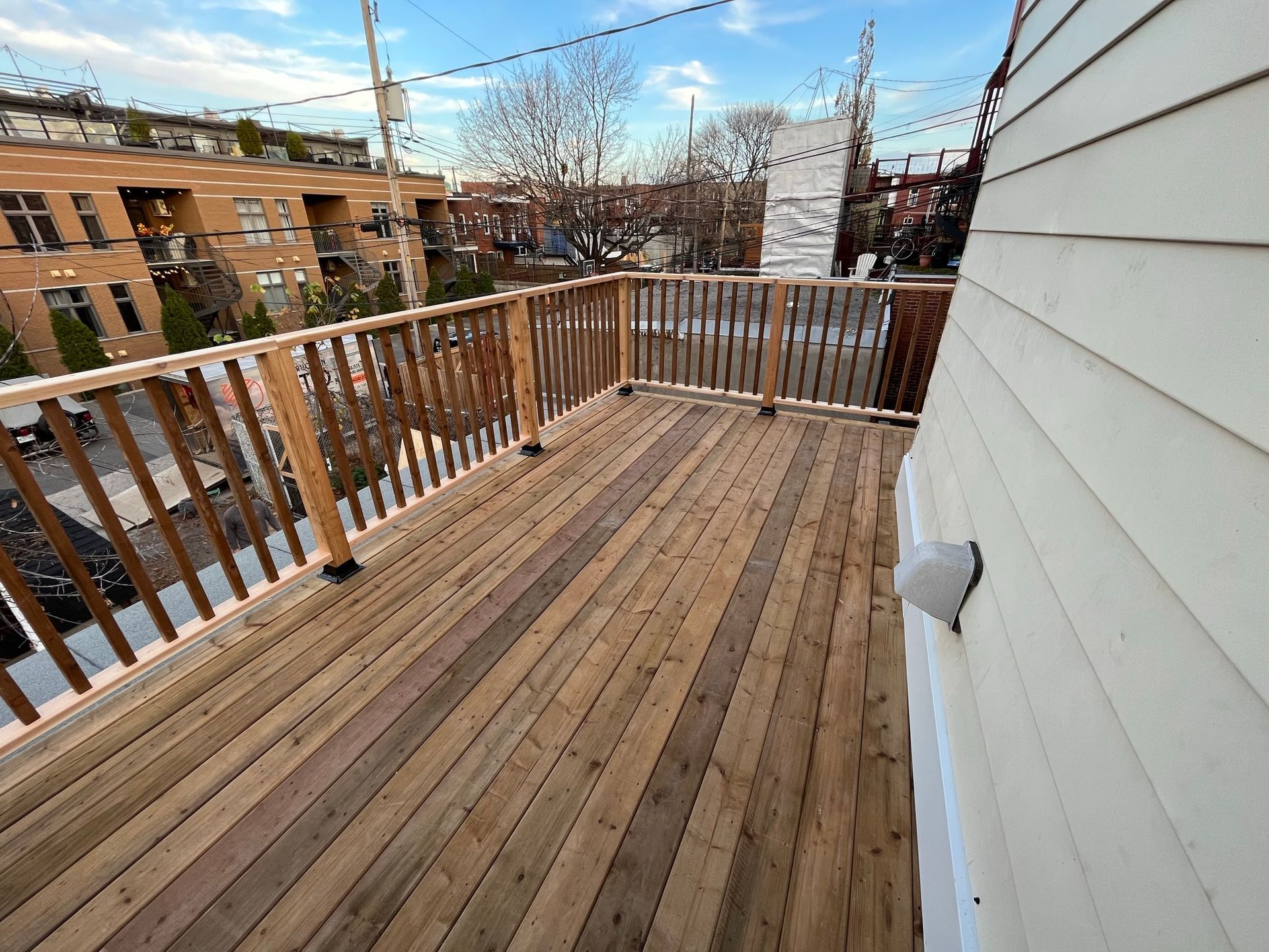Terrasse en bois avec balustrade en bois sur un toit urbain, entour&eacute;e de b&acirc;timents r&eacute;sidentiels.