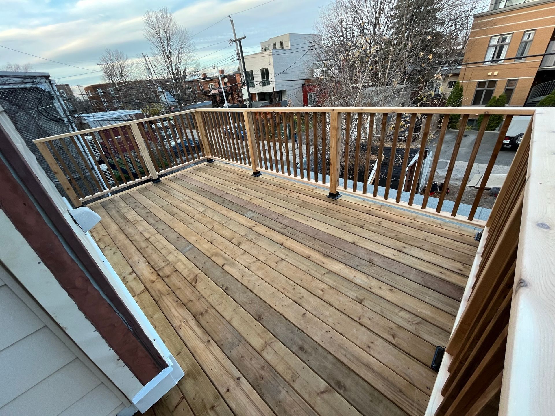 Vue en plongée d'une nouvelle terrasse en bois avec une rambarde assortie, donnant sur une rue de banlieue au crépuscule.
