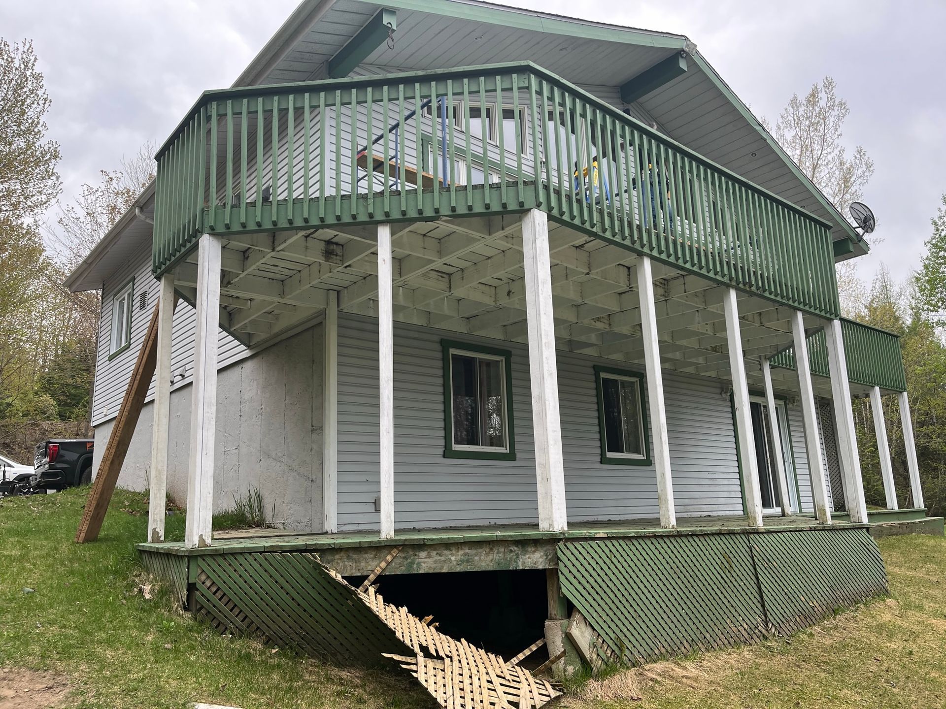 Une maison blanche avec un porche vert et une terrasse cassée.