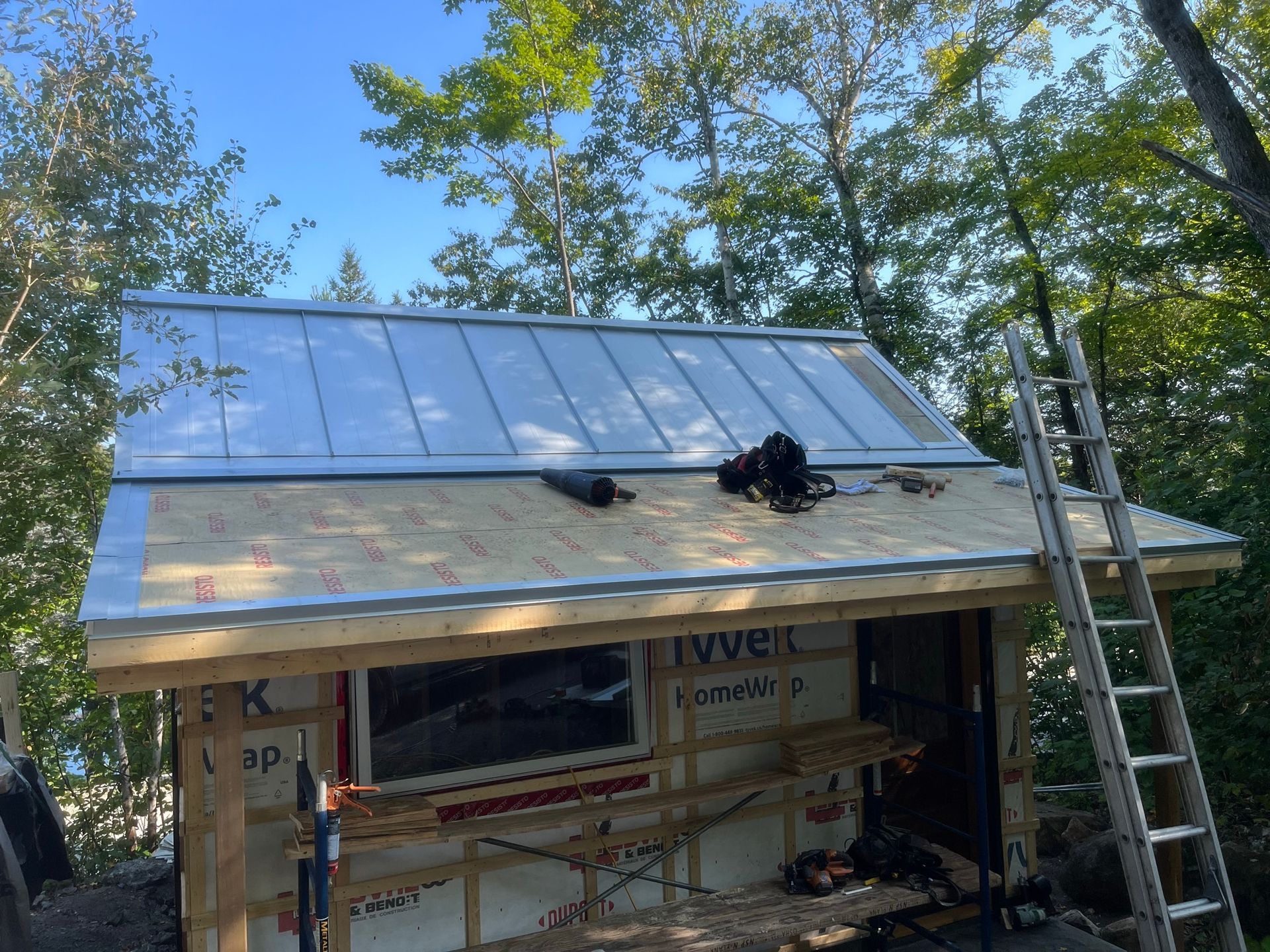 Une échelle est posée au sommet d'un bâtiment en bois avec un toit en métal.