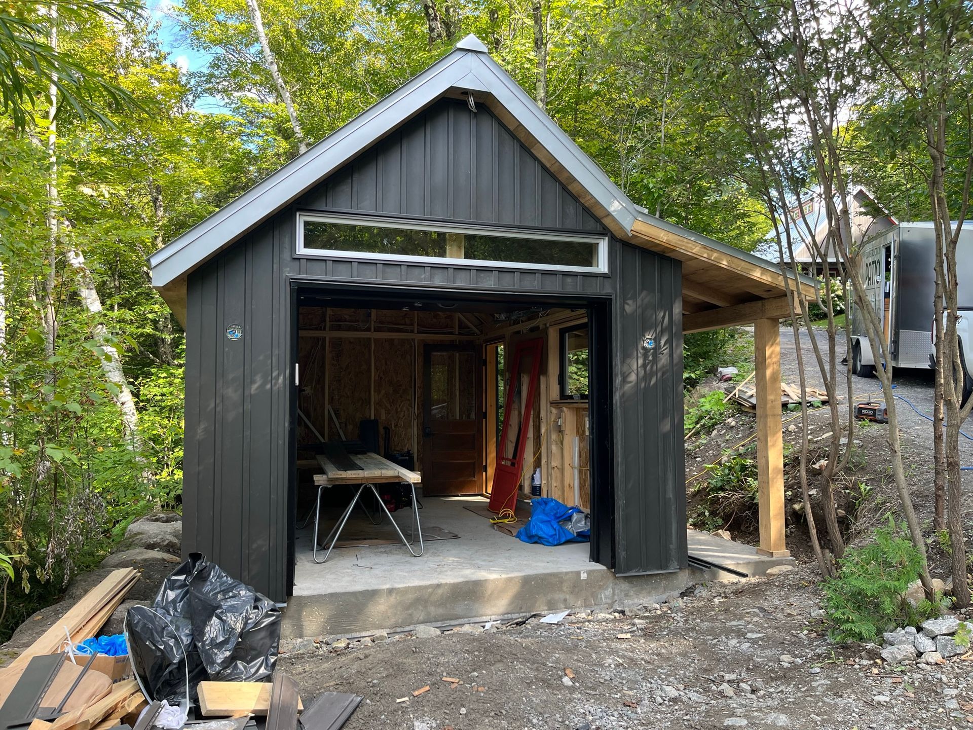 Un hangar noir est en construction au milieu d'une forêt.