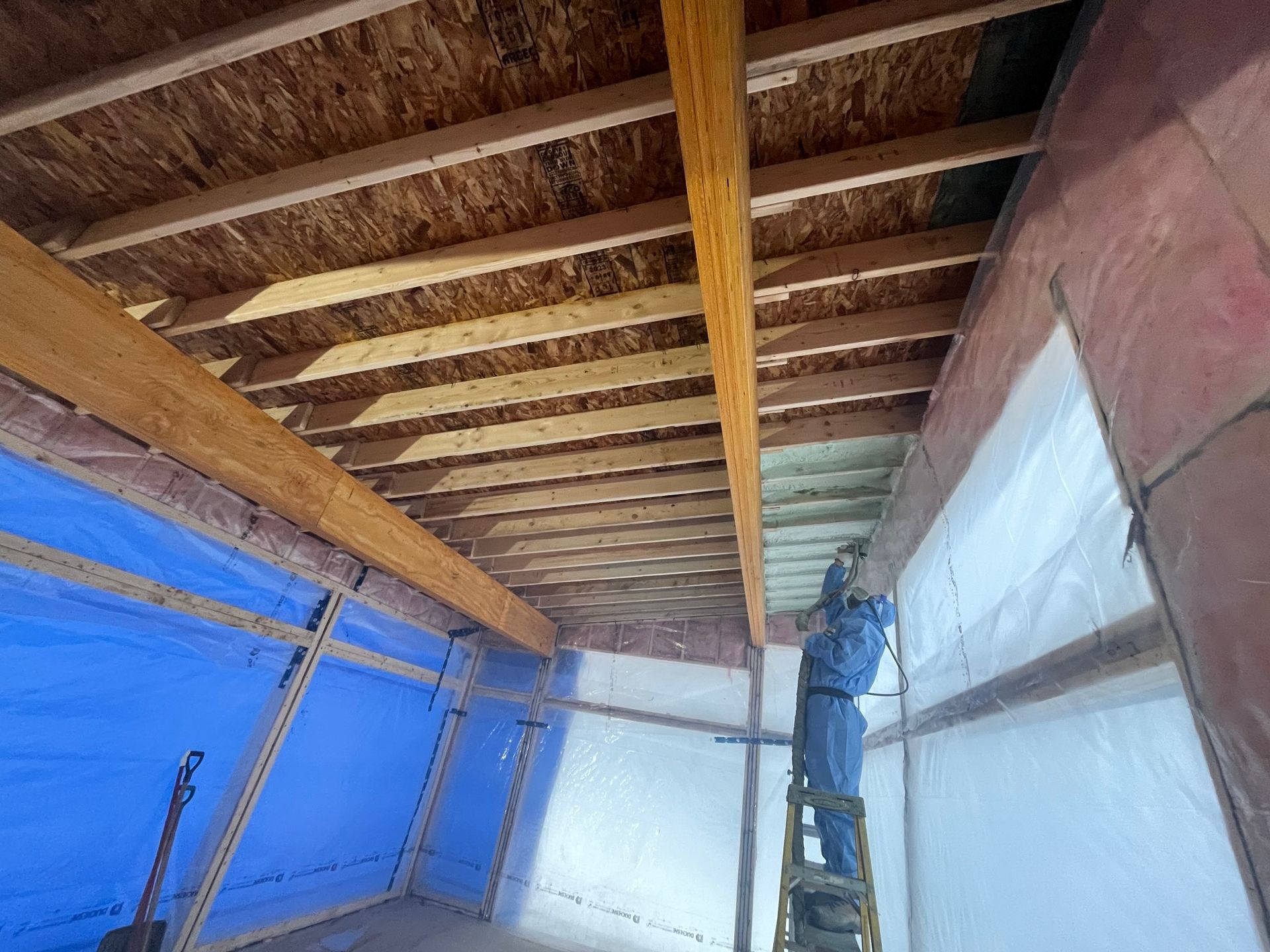 Un homme pulvérise de l'isolant sur le plafond d'un bâtiment.