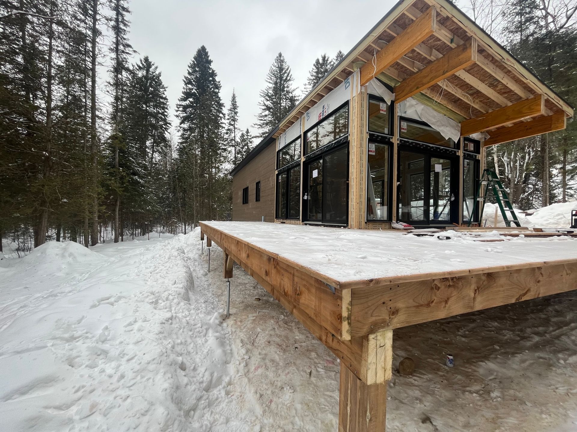 Une maison est en construction dans la neige avec une terrasse en bois devant.