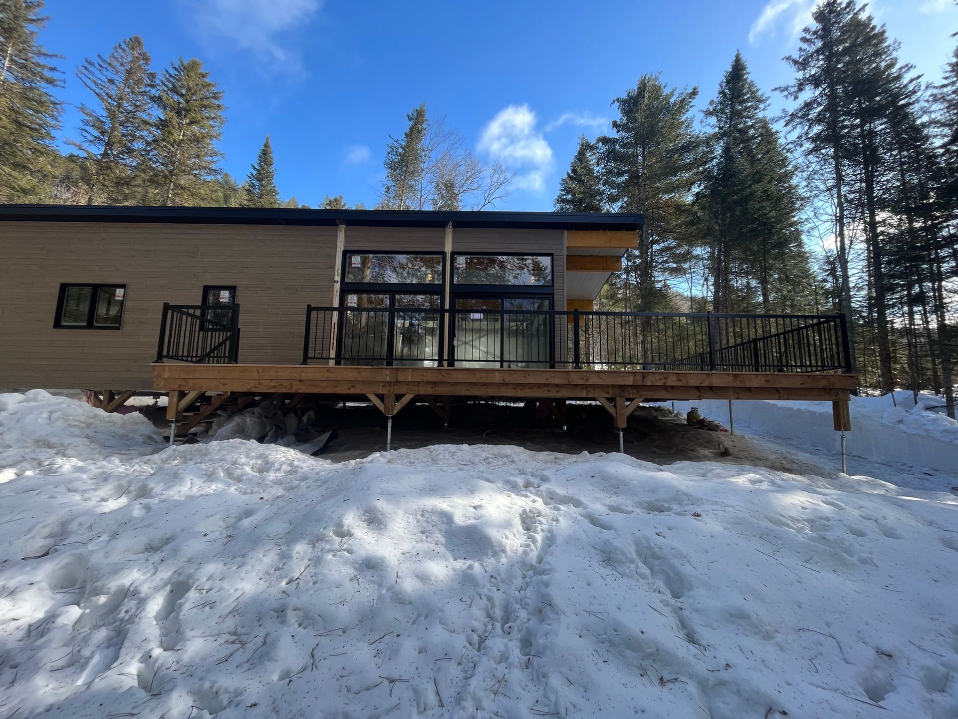 Une maison avec une grande terrasse est entourée de neige et d'arbres.