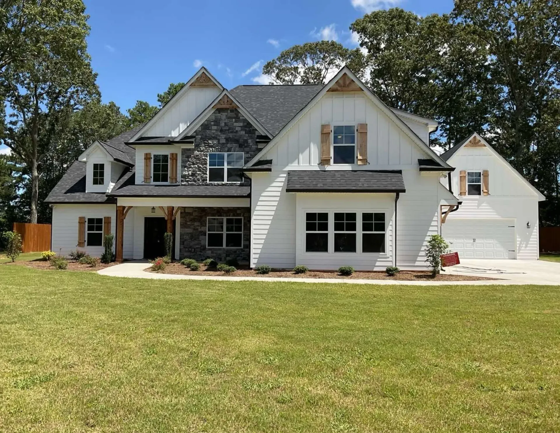 Large white two-story suburban house with a front porch, garage, and wide green lawn under trees