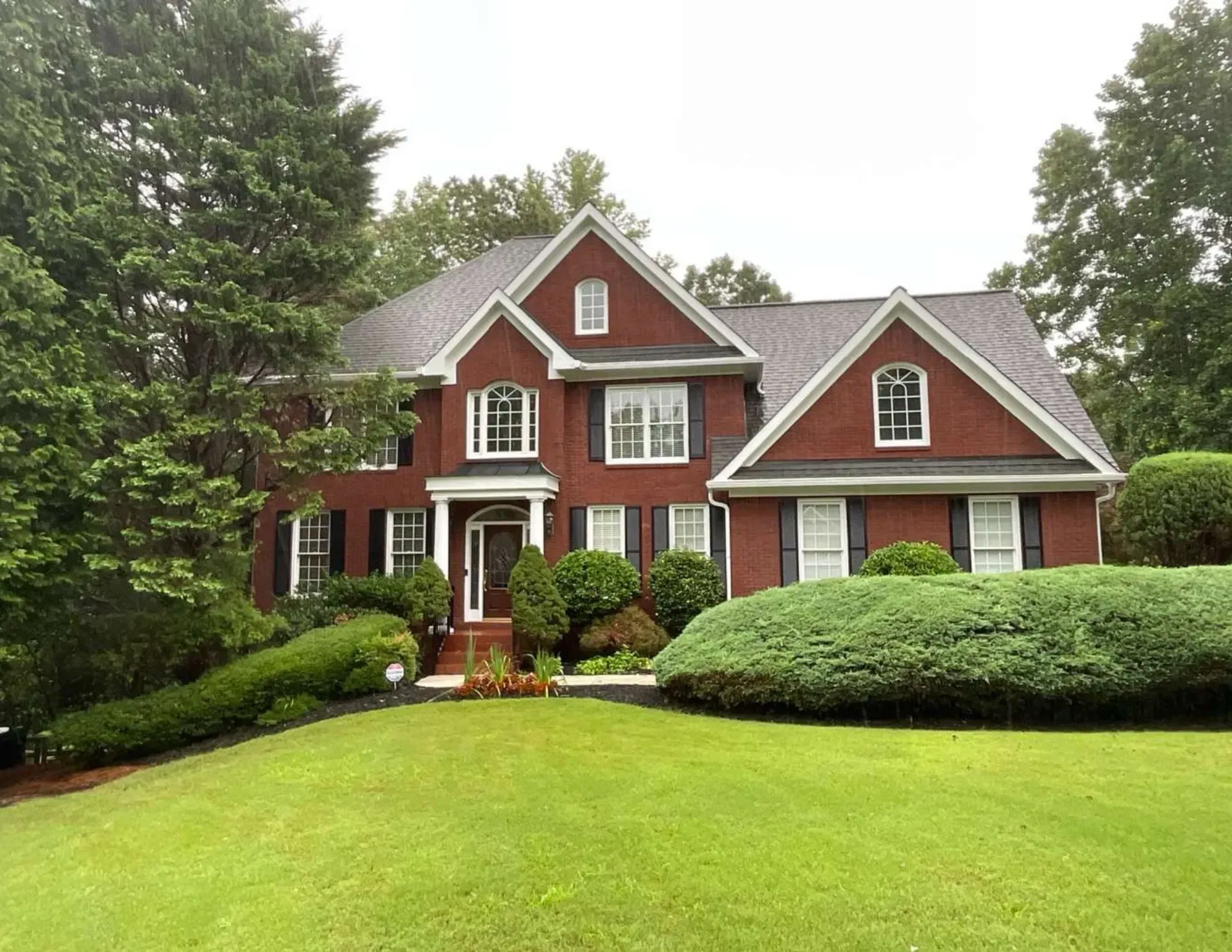 Large red two-story house with white trim, surrounded by green lawn, shrubs, and trees