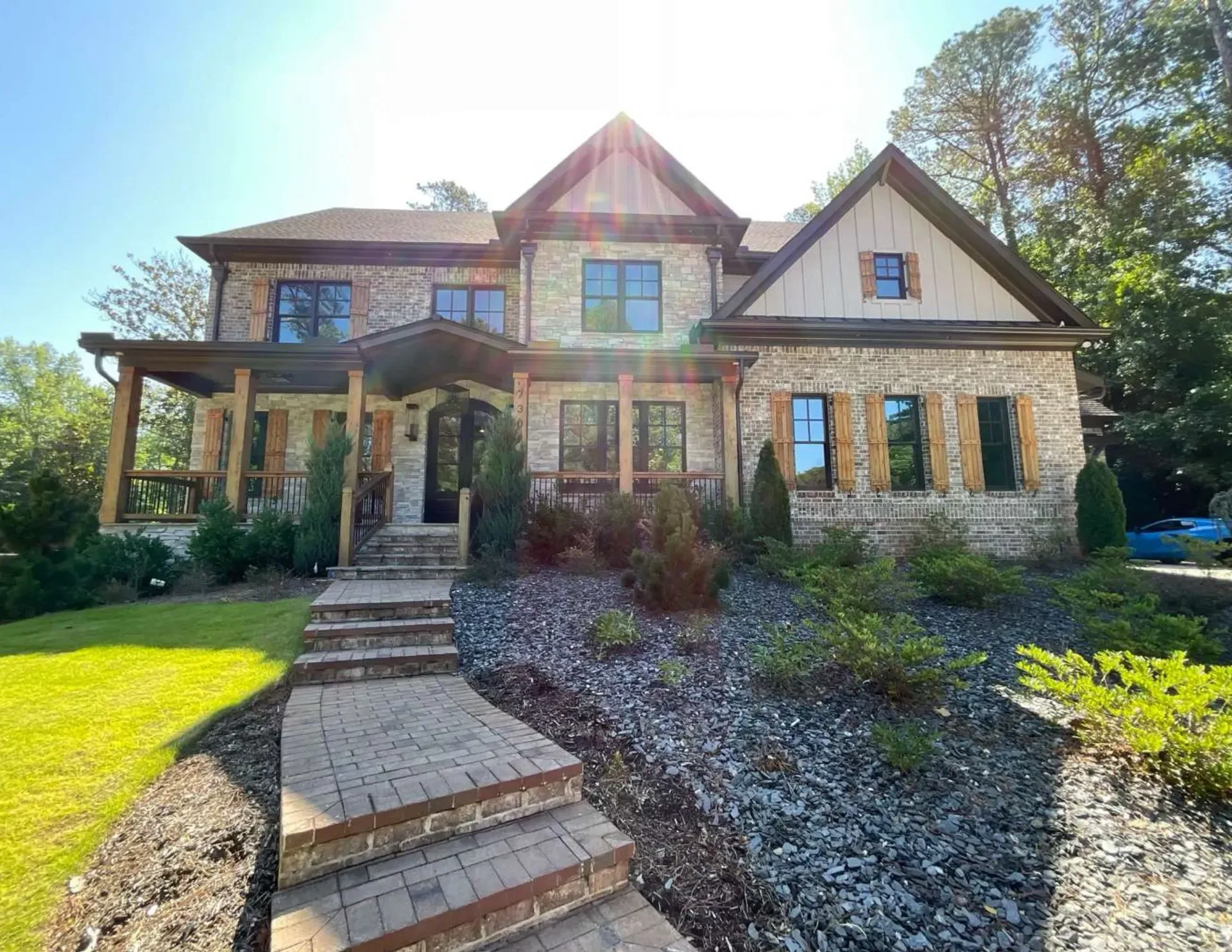 Two-story house with stone façade, front steps, and landscaped yard in bright sunlight