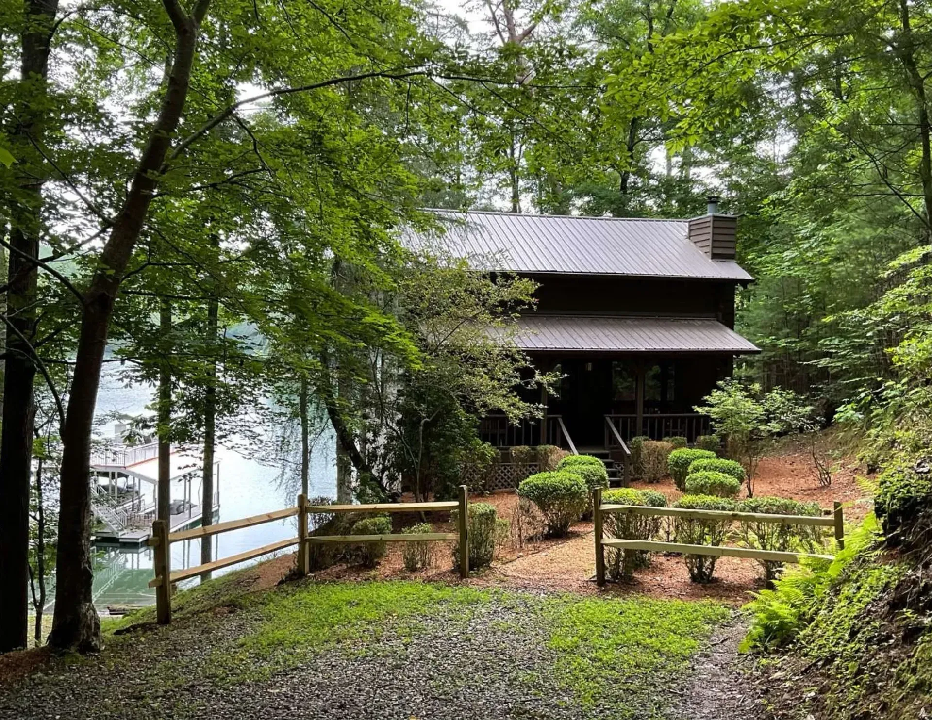 Rustic cabin nestled in a wooded lakeside forest with gravel path and wooden railing.