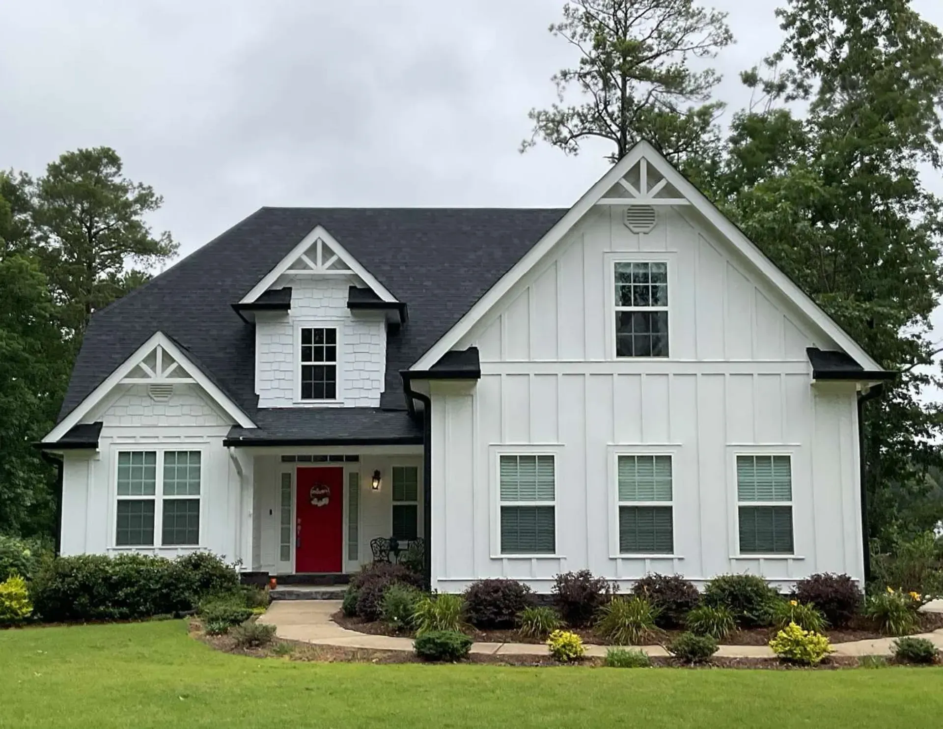 White house with dark roof, red front door, and landscaped front yard under cloudy skies