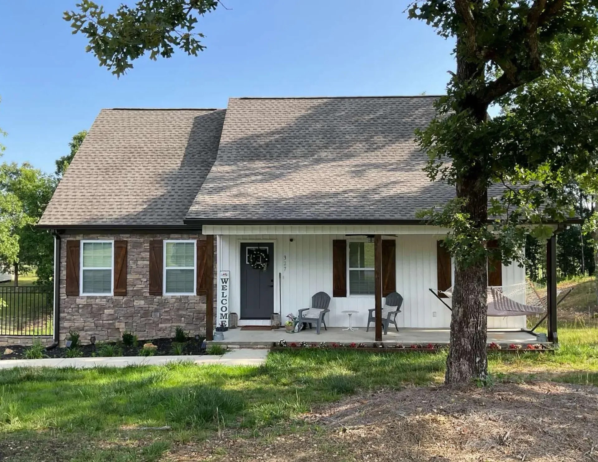 Brick house with front porch, white trim, and shaded yard under trees