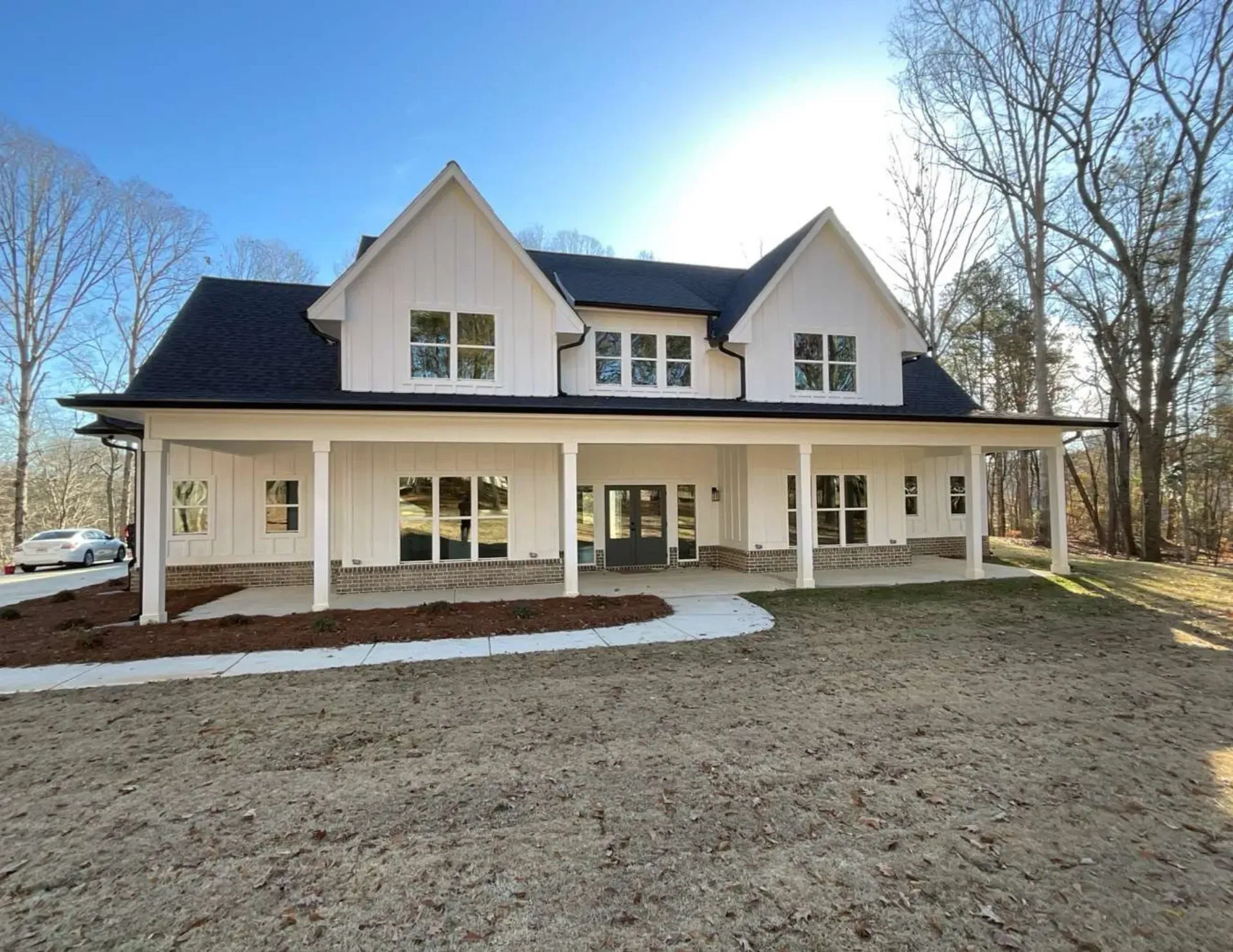 Large white two-story house with a covered porch, dark roof, and bare trees in a yard