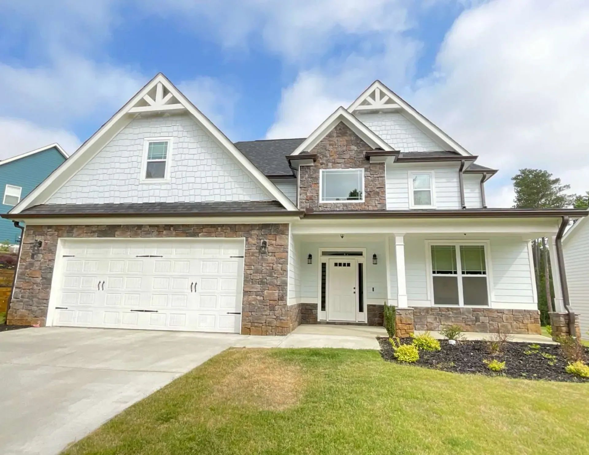 Two-story gray house with white trim, front porch, garage, and manicured lawn