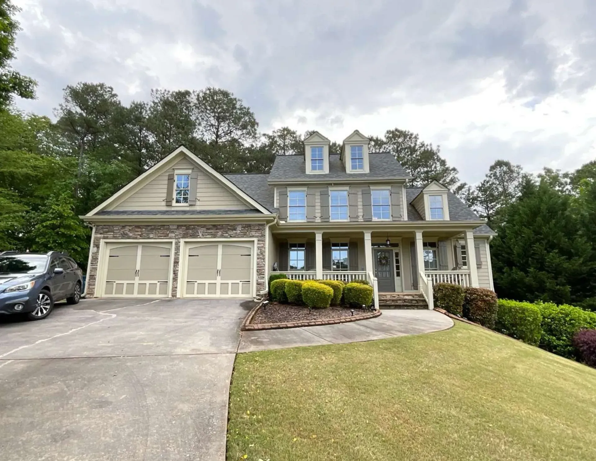 Large gray suburban house with garage, front porch, driveway, and manicured lawn under cloudy sky