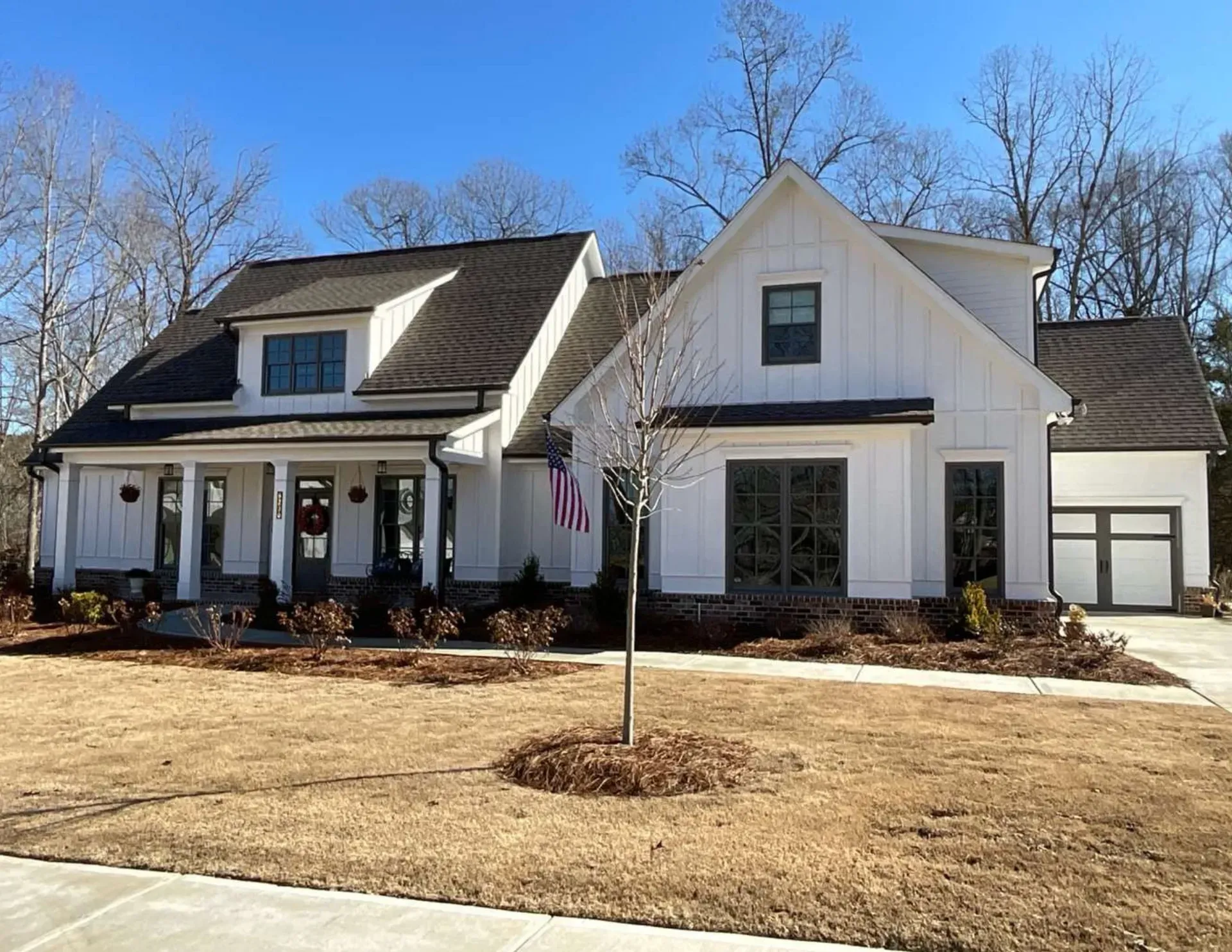 White suburban house with black roof, front porch, and a detached garage under a clear blue sky