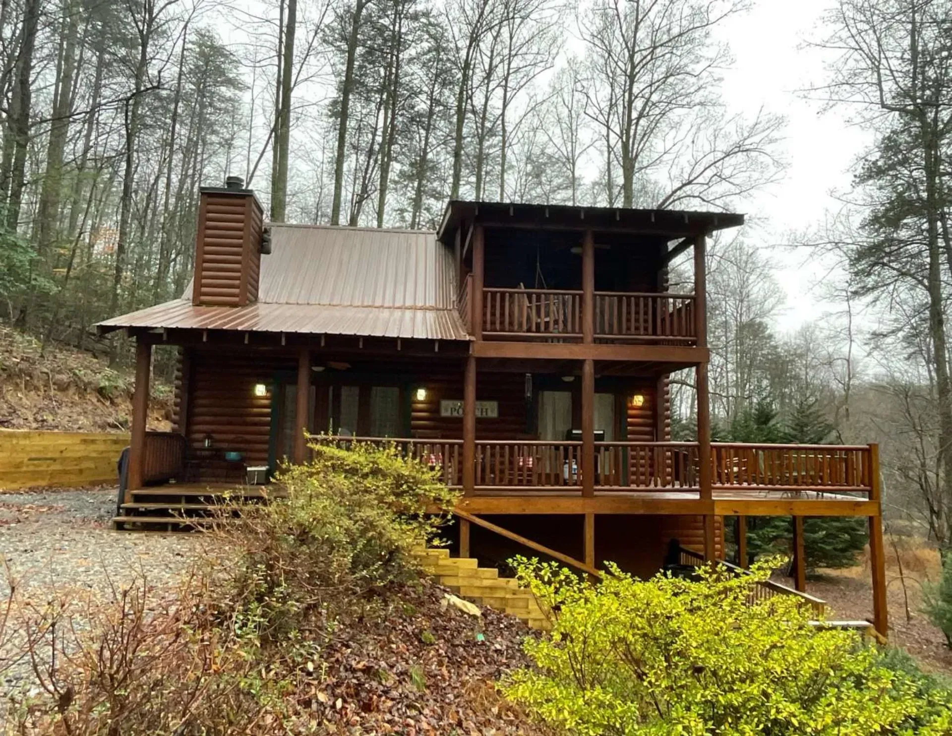 Rustic log cabin with a wooden deck in a wooded hillside setting