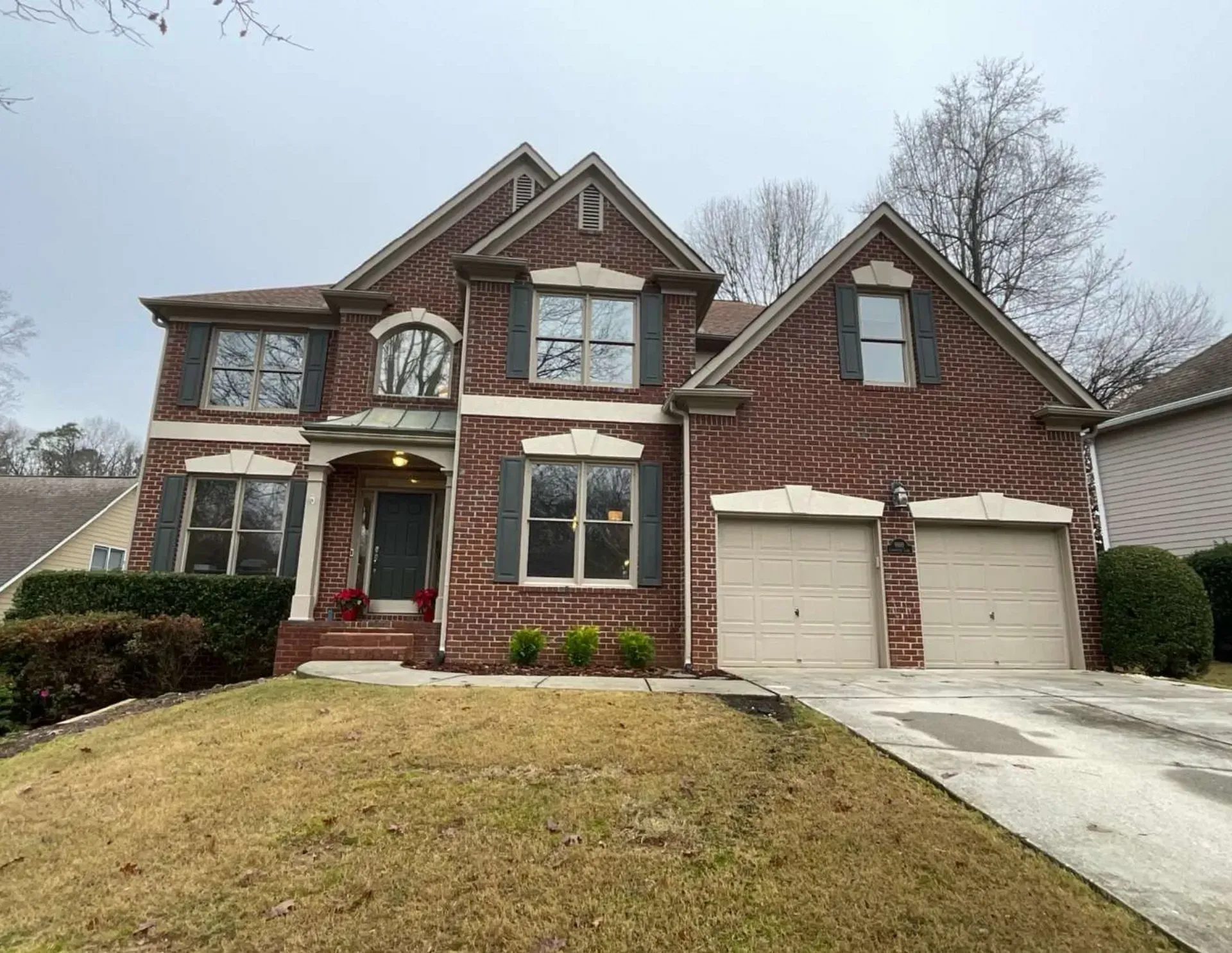 Two-story brick house with a double garage and a front lawn on a cloudy day