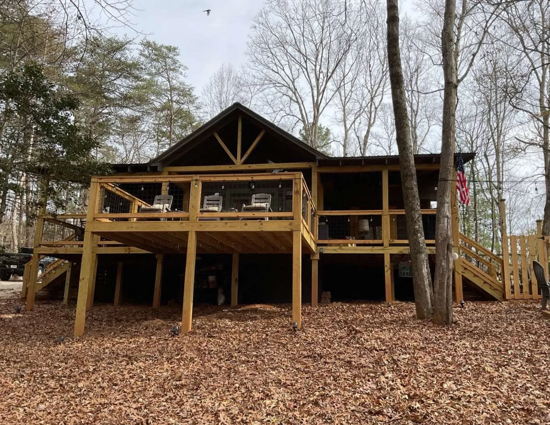 Wooden cabin with wraparound deck in a leaf-covered wooded area
