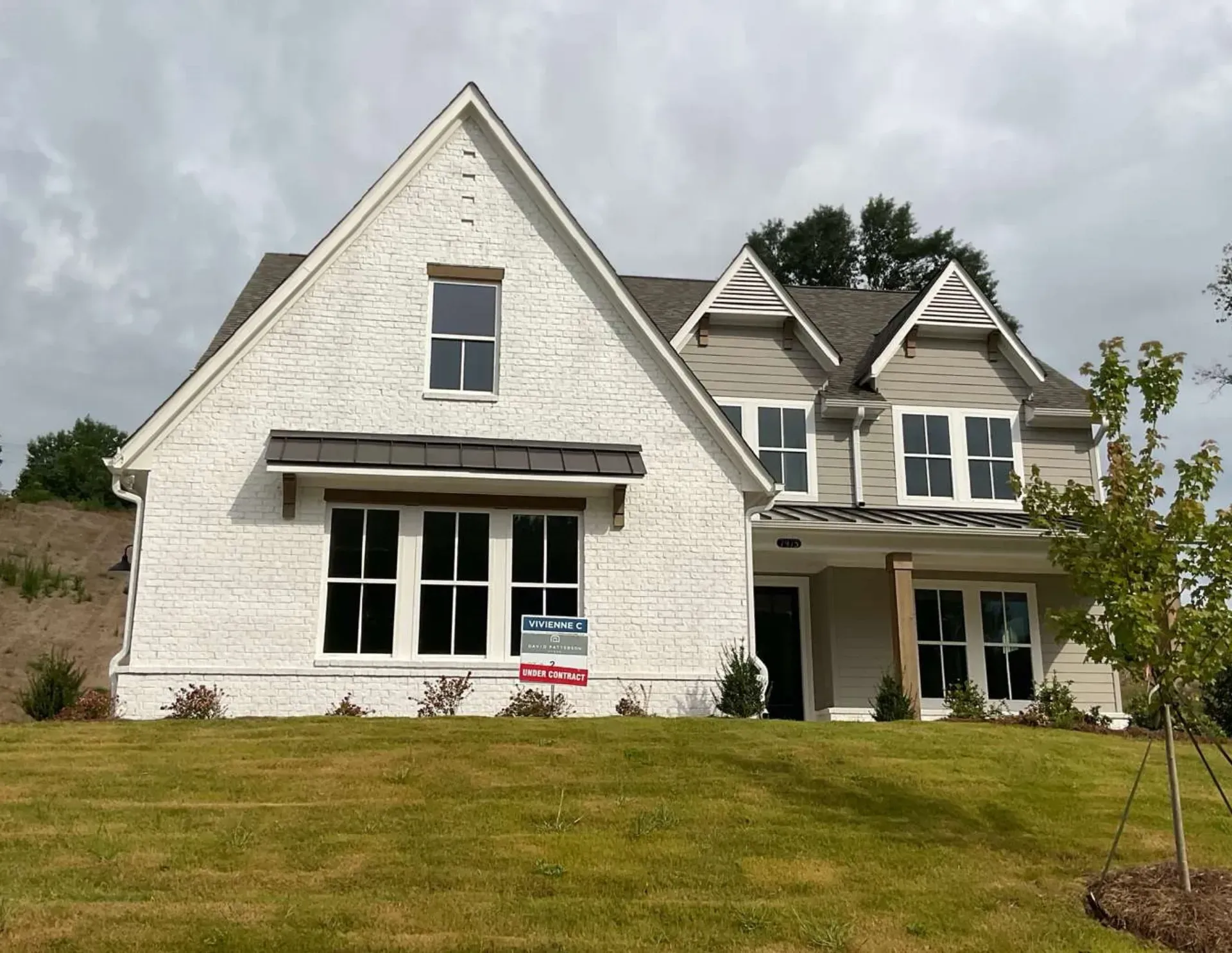 Large white suburban house with steep gables and a front lawn under a cloudy sky